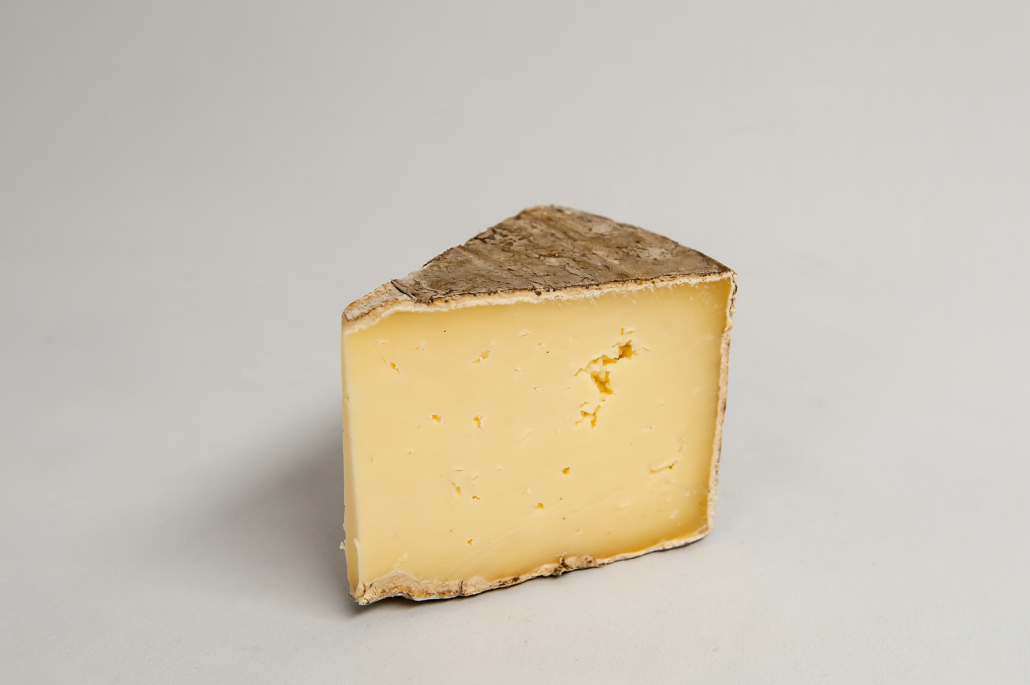 a wedge of buttery coloured cheese with a speckled grey rind