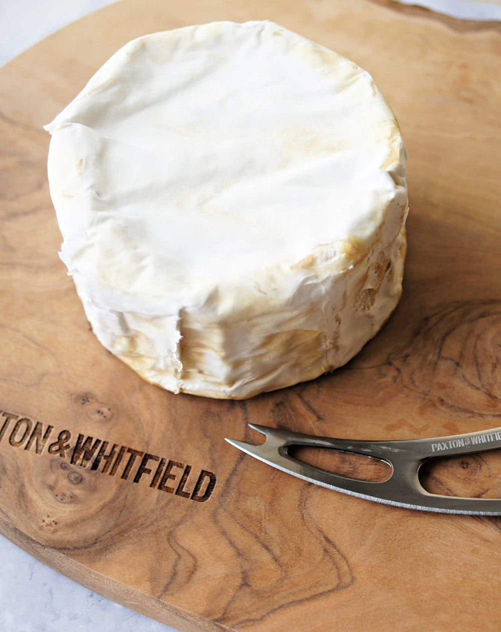 close up of celtic soft cheese on a wooden paxton and whitfield cheeseboard 