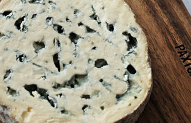 close up of fourme d'ambert blue cheese on paxton and whitfield wooden cheeseboard and cheese knife