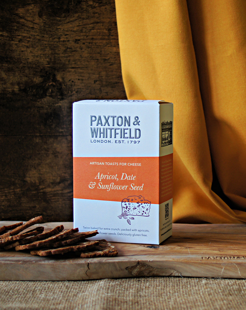 box of paxton and whitfield apricot date and sunflower seed artisan toasts for cheese on wooden cheeseboard