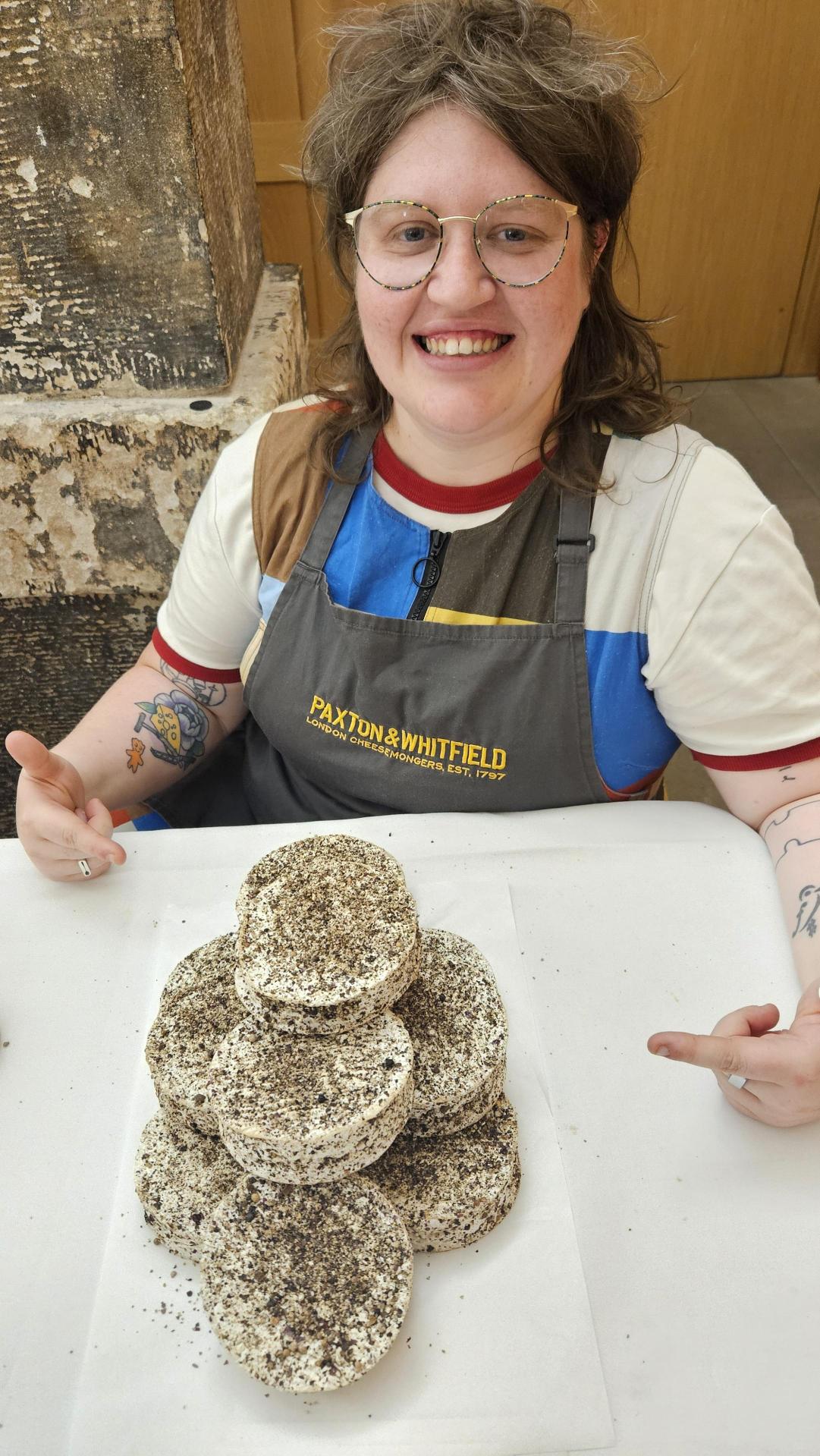 Person wearing an apron with a stack of pepper encrusted cheeses on a table