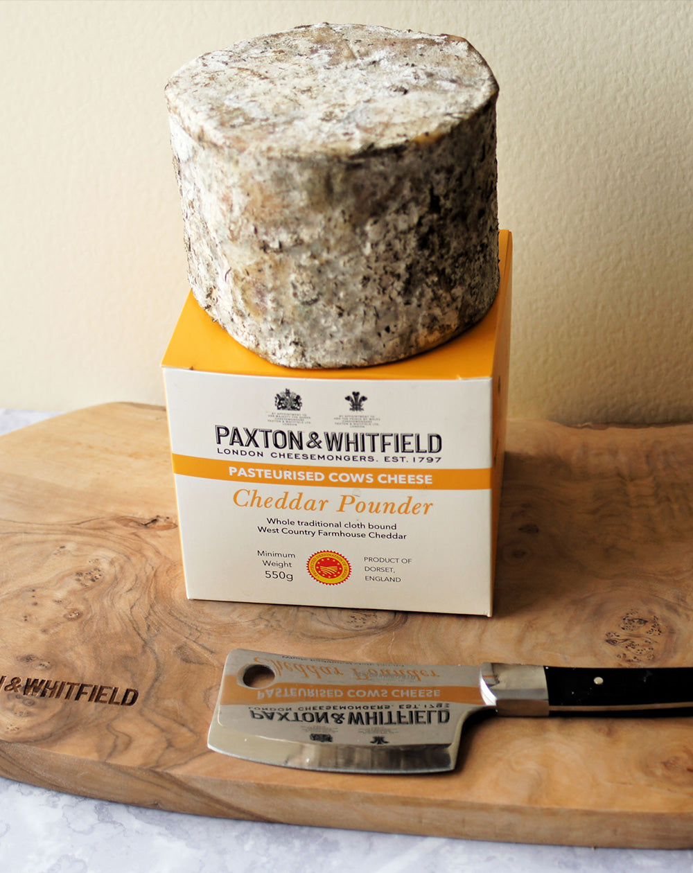 paxton and whitfield cheddar pounder cheese with box packaging on wooden cheeseboard with cheese knife